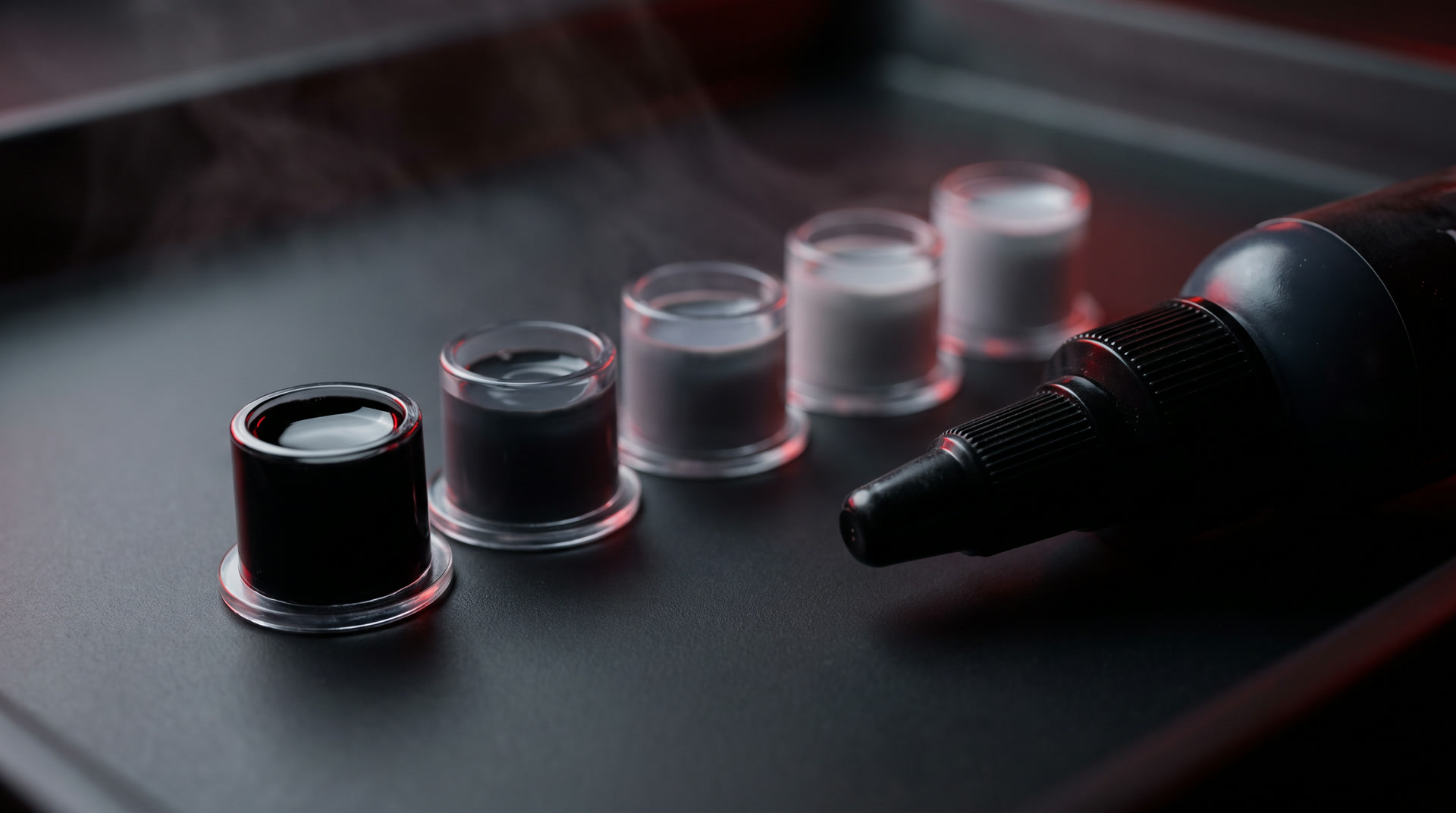 A row of ink caps holding a greywash scale from pure black to pale silver, under amber light