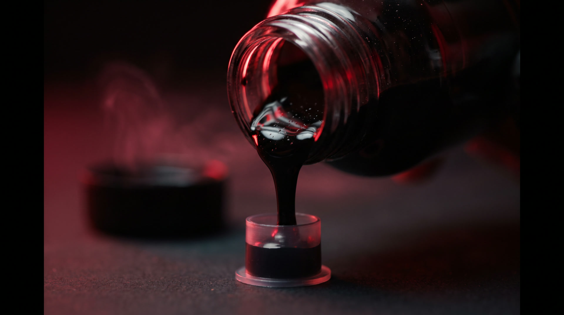 Black tattoo ink pouring from a bottle into an ink cap under amber light