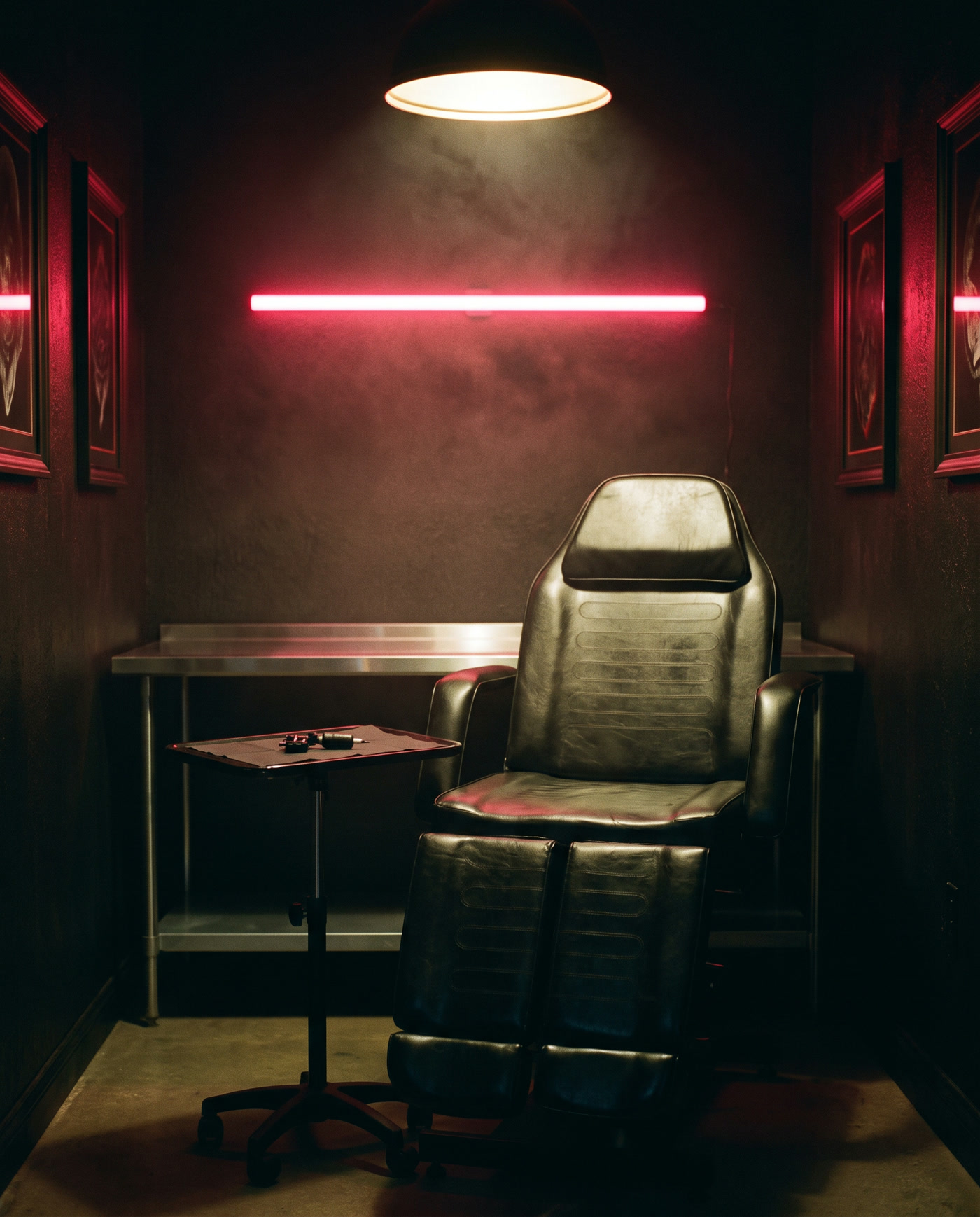 The studio: an empty tattoo chair under a warm light, steel workstation, and amber neon on the wall